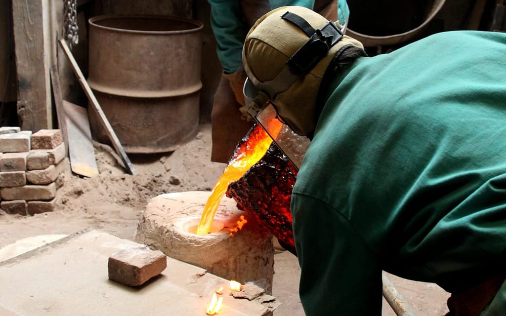 Dexter pouring molten bronze from a crucible into a plaster mold in his foundry.