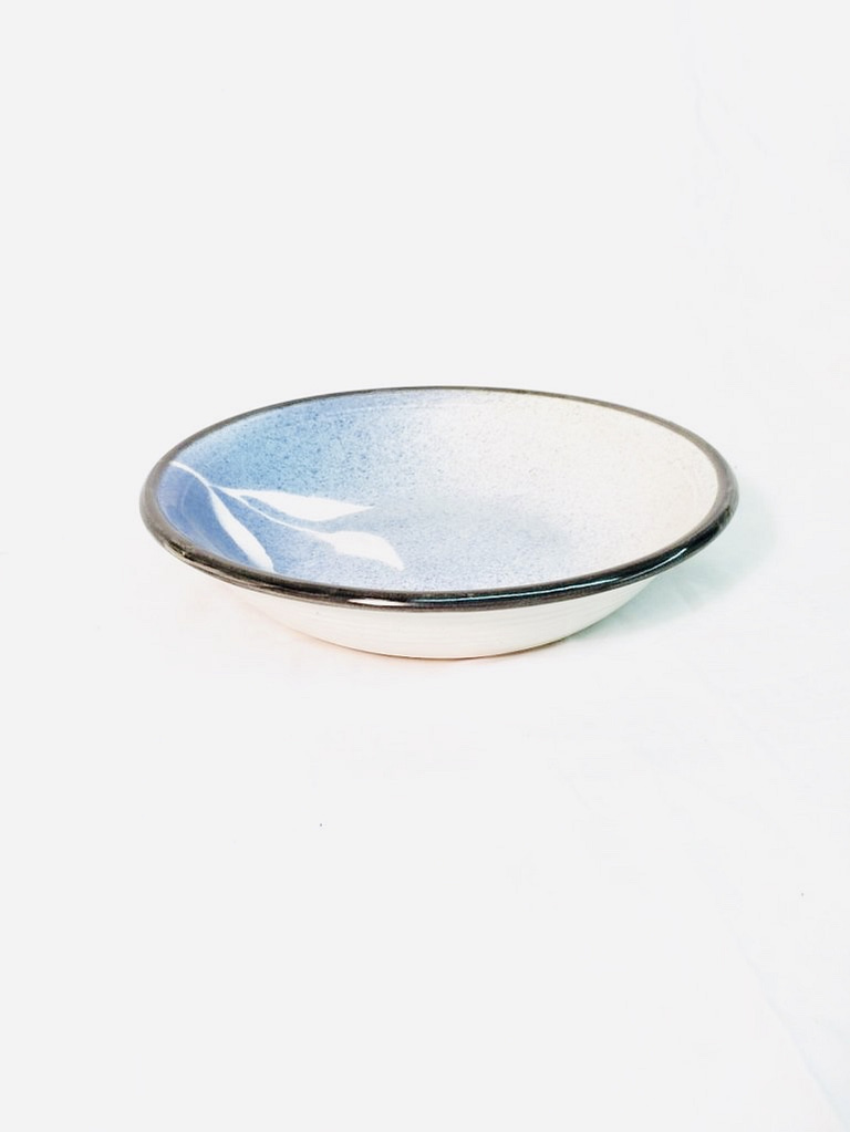 A bowl glazed with blues and a black rim. It has a leaf stencil pattern