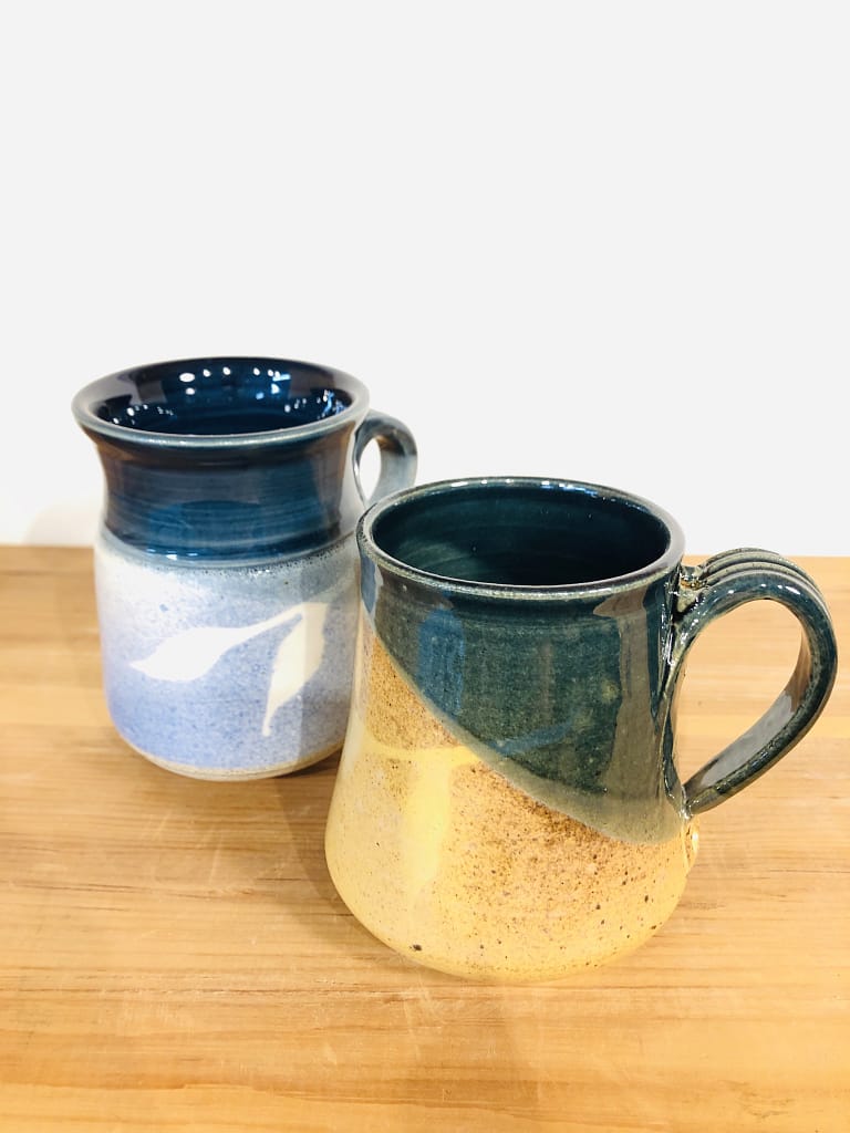 One mug glazed in light and dark blue, and another mug glazed with gold and dark green
