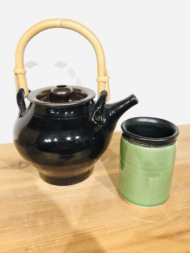 A black teapot with a green mug. the mug has a black rim and interior
