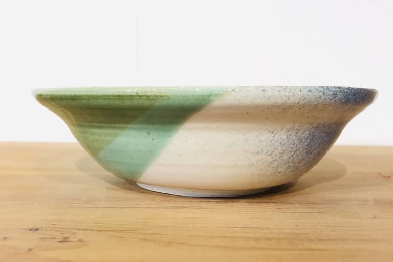 Profile side view of a shallow bowl glazed with greens and blues