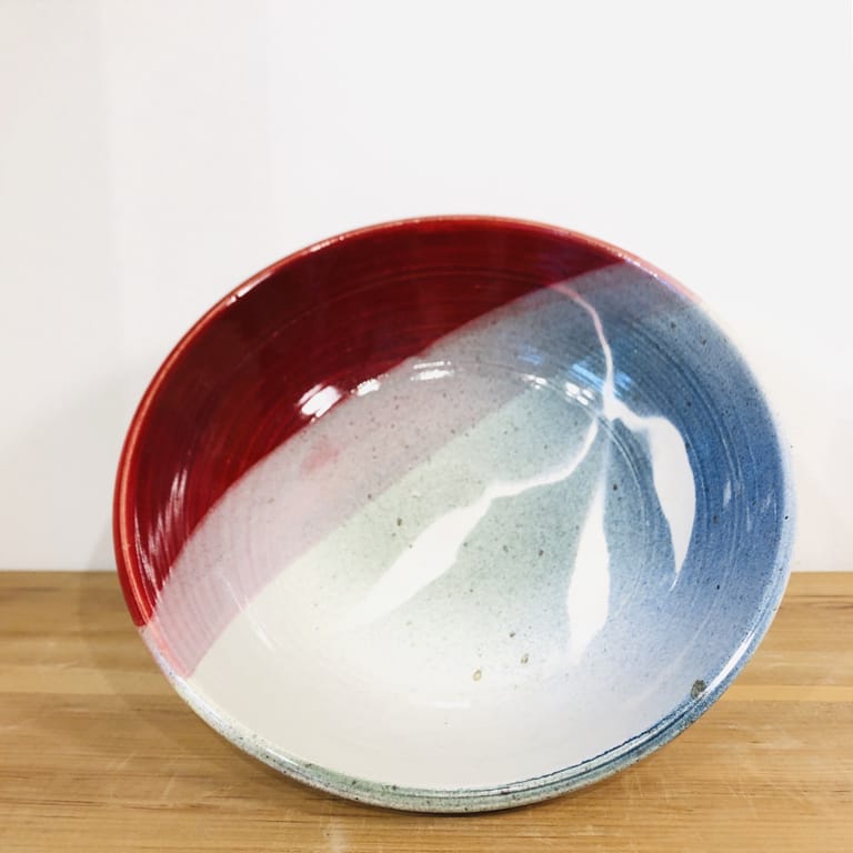 A blue bowl dipped in deep firebrick red on one side with a leaf stencil pattern