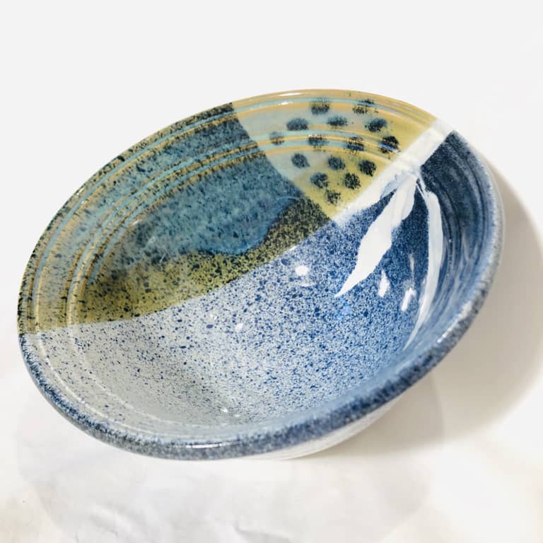A small blue salad bowl with a speckled routil blue glaze and stenciled leaf