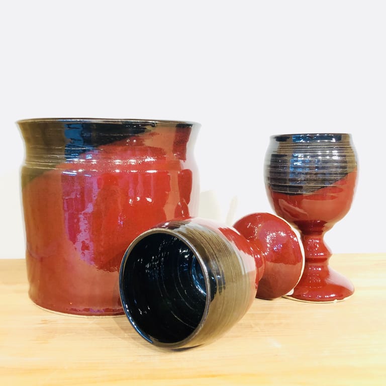 A matching pair of wine goblets with an ice cooler, all glazed in deep firebrick red and black.