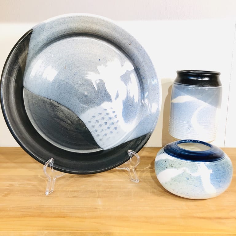 A platter with one tall cylindrical vase and one short spherical vase. All are glazed with shades of blues and black.