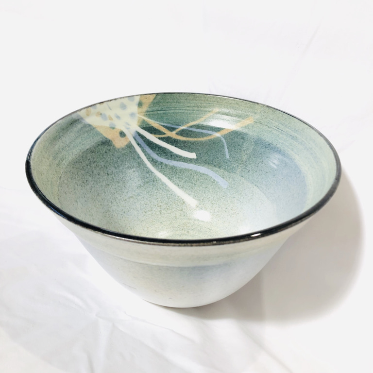 A large, deep turquoise salad bowl with a colorful stenciled ribbon pattern inside